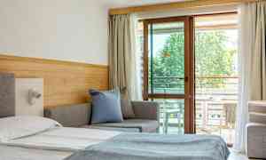 Et hotellrom med en seng, sofa og balkongmøbler synlige gjennom en glassdør. (AI-generert tekst)