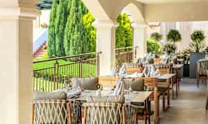 Uteservering med bord dekket og stoler i en frodig omgivelser. (AI-generert tekst)