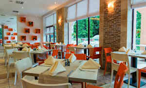 Fotografi av en innendørs restaurant med dekkede bord og stoler i forskjellige farger. (AI-generert tekst)