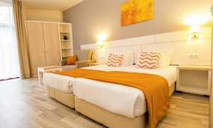 Et lyst hotellrom med to senger, orange detaljer og møbler. (AI-generert tekst)