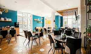 En lyst og moderne innredet kafé med blå vegger, hexagonformet tregulv og flere bord med komfortable stoler. (AI-generert tekst)