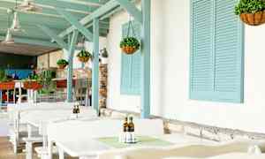 Utendørs sitteområde med hvite bord, hengende planter og blå tretapper. (AI-generert tekst)