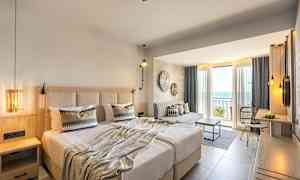 Hotellrom med dobbeltseng, sitteområde og balkong med utsikt over havet. (AI-generert tekst)