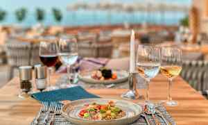 Et dekket restaurantbord med en tallerken mat og glass med vin, vann og et tent lys. (AI-generert tekst)