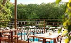 Utendørs servering med bord og stoler samt utsikt over bassengområde og grøntområder. (AI-generert tekst)