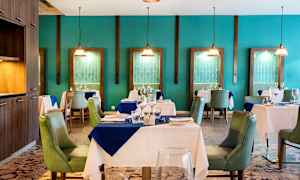 Et elegant restaurantinteriør med dekket bord og grønne stoler, omgitt av turkise vegger og dekorative hengelamper. (AI-generert tekst)