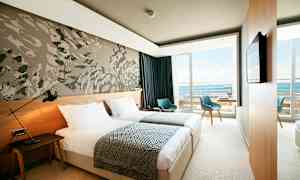 Et moderne hotellrom med to enkeltsenger, en veggdekorasjon og en balkong med utsikt over havet. (AI-generert tekst)