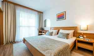 Et hotellrom med en dobbeltseng, en skrivebordsstol, et vindu med gardiner og et veggdekor. (AI-generert tekst)