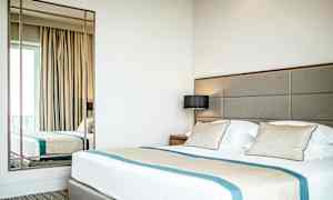 Et hotellrom med en stor seng, puter og et speil. (AI-generert tekst)