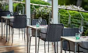 En uteservering med bord og stoler dekket med glass og servietter. (AI-generert tekst)