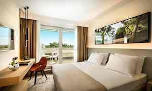 Hotellrom med en seng, skrivebord og stol, samt en balkong med utemøbler. (AI-generert tekst)