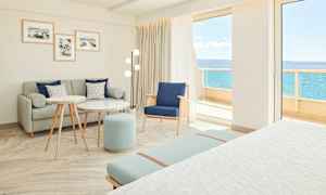 Lyst og moderne hotellrom med sittegruppe og utsikt mot havet. (AI-generert tekst)