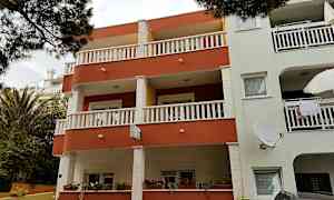 Leilighetsbygg med balkonger og vinduer, omgitt av planter. (AI-generert tekst)