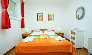 Et soverom med en dobbeltseng og oransje sengeteppe, to nattbord med lamper og veggdekorasjoner. (AI-generert tekst)