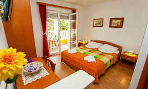 Et rom med en dobbeltseng, bord, stoler og en åpnet balkongdør. (AI-generert tekst)