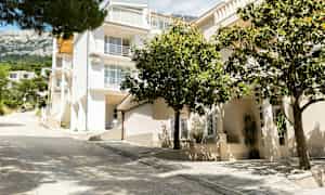 Hvit bygning med flere etasjer og balkonger, omgitt av grøntområder. (AI-generert tekst)