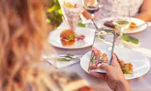 Person tar bilde av tallerken med mat på utendørsbord. (AI-generert tekst)