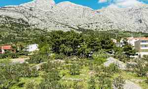 Bilde av et landskap med bygninger, trær og grøntområder foran fjell. (AI-generert tekst)