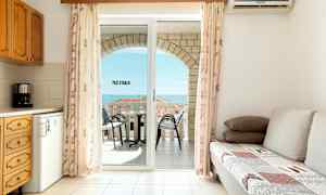 En stue med en sovesofa, et kjøkken og en balkong med utsikt over havet. (AI-generert tekst)