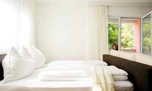 Et lyst rom med en seng nær vindu og balkong. (AI-generert tekst)