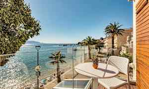 Utsikt fra en balkong mot en solfylt strand med palmer og klart vann. (AI-generert tekst)