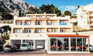 En bygning med teksten 'Villa Palloma' øverst, med balkonger og parkerte biler foran. (AI-generert tekst)