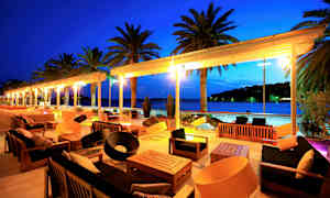 Utendørsmøbler på en terrasse med utsikt over havet og palmer om kvelden. (AI-generert tekst)