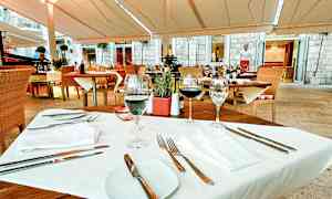 Et bord dekket for middagsgjester på en uterestaurant med tremøbler og hvite tekstiler. (AI-generert tekst)