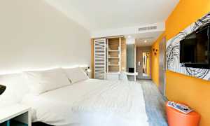 Et moderne hotellrom med en stor seng med hvitt sengetøy, oransje og hvite vegger, en veggmontert TV og et skrivebord. (AI-generert tekst)