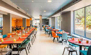En moderne spisesal med store vinduer, fargerike stoler og dekkede bord. (AI-generert tekst)