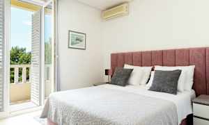 Et lyst soverom med rosa sengegavl, hvitt sengeteppe og en dør ut til en balkong. (AI-generert tekst)