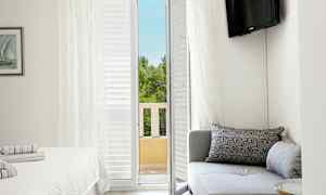 Et hotellrom med en sofa, en seng og en balkongdør som fører ut til utsikt over trær. (AI-generert tekst)