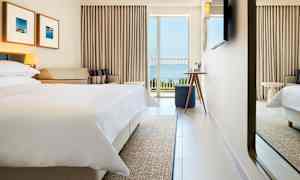 Hotellrom med oppredd seng, sofa og balkong med havutsikt. (AI-generert tekst)