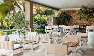 En utendørs terrasse med bord, stoler og en steinmur. (AI-generert tekst)