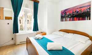 Et soverom med dobbeltseng, turkise gardiner og et bilde av en bysilhuett på veggen. (AI-generert tekst)