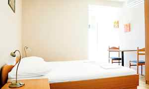 Et enkelt hotellrom med en seng av tre, et nattbord og et bord med to stoler. (AI-generert tekst)