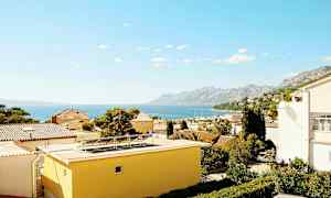 Utsikt over hustak med havet og fjell i bakgrunnen. (AI-generert tekst)