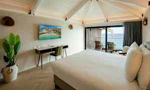 Et hotellrom med en dobbeltseng, skrivebord, TV og balkong med utsikt over havet. (AI-generert tekst)