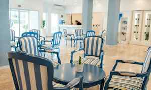 En lys og luftig hotellfoajé med blå og hvitstripete sittemøbler og et rundt bord. (AI-generert tekst)