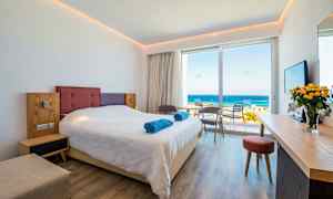 Hotellrom med en dobbeltseng, sittegruppe og utsikt over havet. (AI-generert tekst)