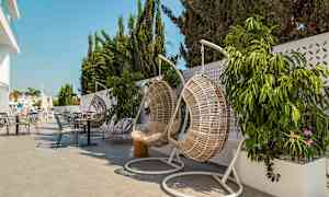 Hengende kurvstoler og bord på en terrasse med planter og parasoller. (AI-generert tekst)