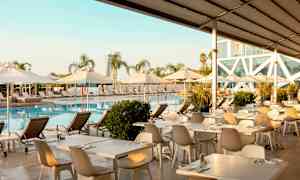 Bassengområde med solsenger, parasoller og spisebord ved vannet. (AI-generert tekst)