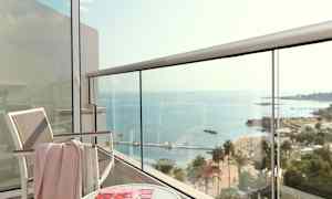 Utsikt fra en balkong mot havet, med en stol, et bord og et magasin. (AI-generert tekst)