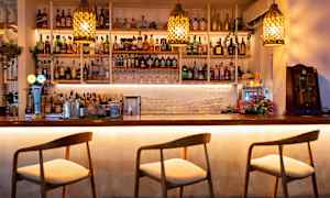 En bardisk med stoler og hyller fylt med flasker og glass. (AI-generert tekst)