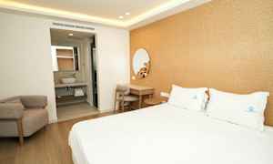 Et hotellrom med en dobbeltseng, et skrivebord og en lenestol. I bakgrunnen er et baderom. (AI-generert tekst)