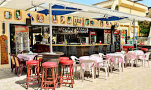 En utendørs servering med bord, stoler og en bar. (AI-generert tekst)