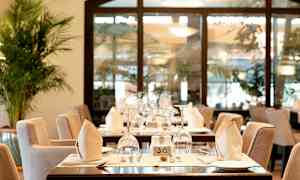 Et restaurantbord med elegant borddekking som inkluderer glass, tallerkener og brettede servietter. (AI-generert tekst)