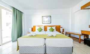 To enkeltsenger med grønn sengeteppe og hvite puter i et hotellrom med lys innredning. (AI-generert tekst)