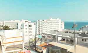 Utsikt fra en balkong med stoler og et bord, med hotellbygninger og havet i bakgrunnen. (AI-generert tekst)