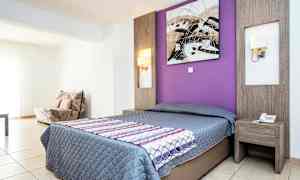 Et hotellrom med en dobbeltseng, en lilla vegg bak sengen og et sidebord. (AI-generert tekst)